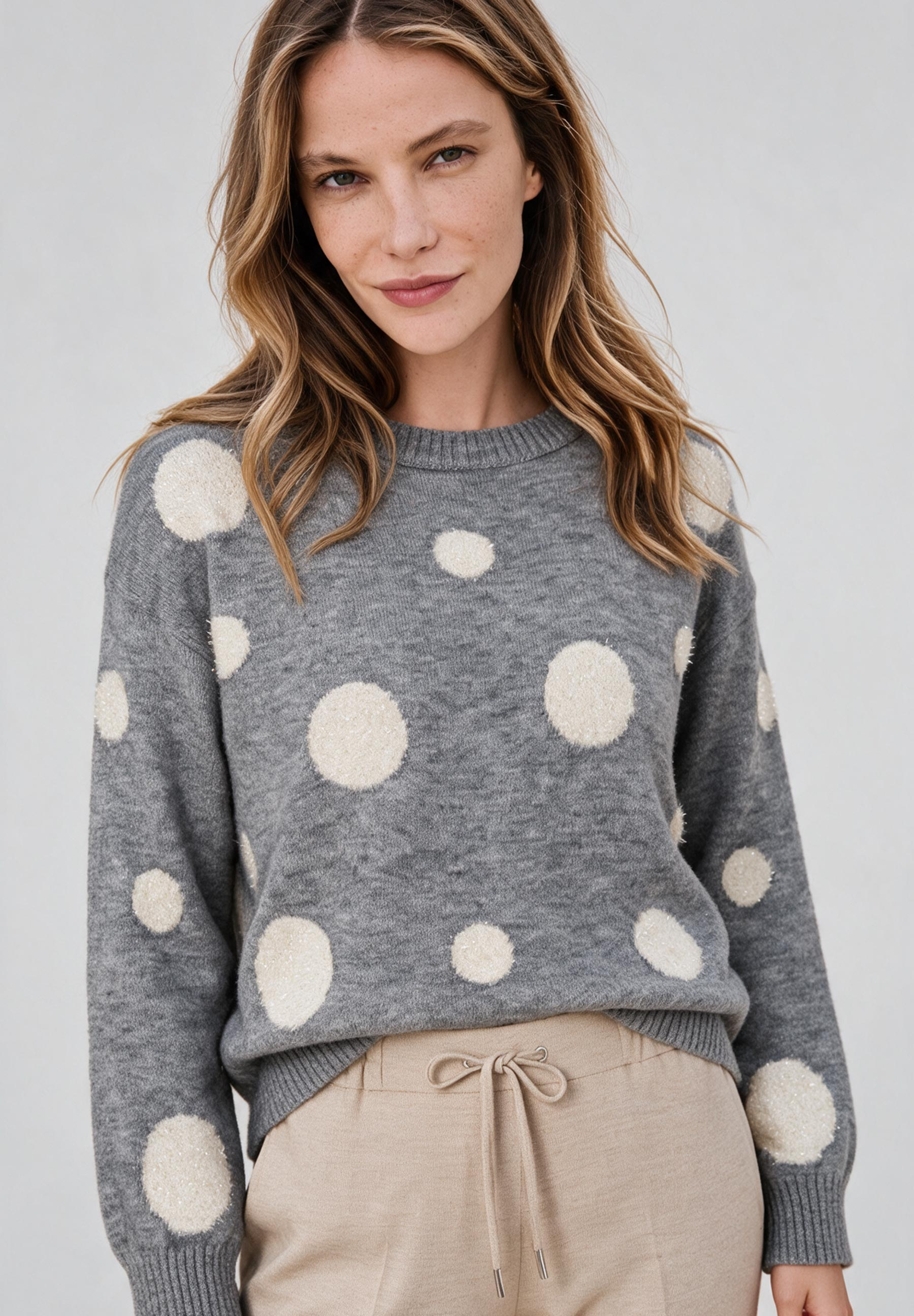 AI generated - MORE & MORE Pullover: Eine Frau trägt einen grauen Strickpullover mit beigefarbenen Punkten und eine beigefarbene Hose mit Kordelzug.