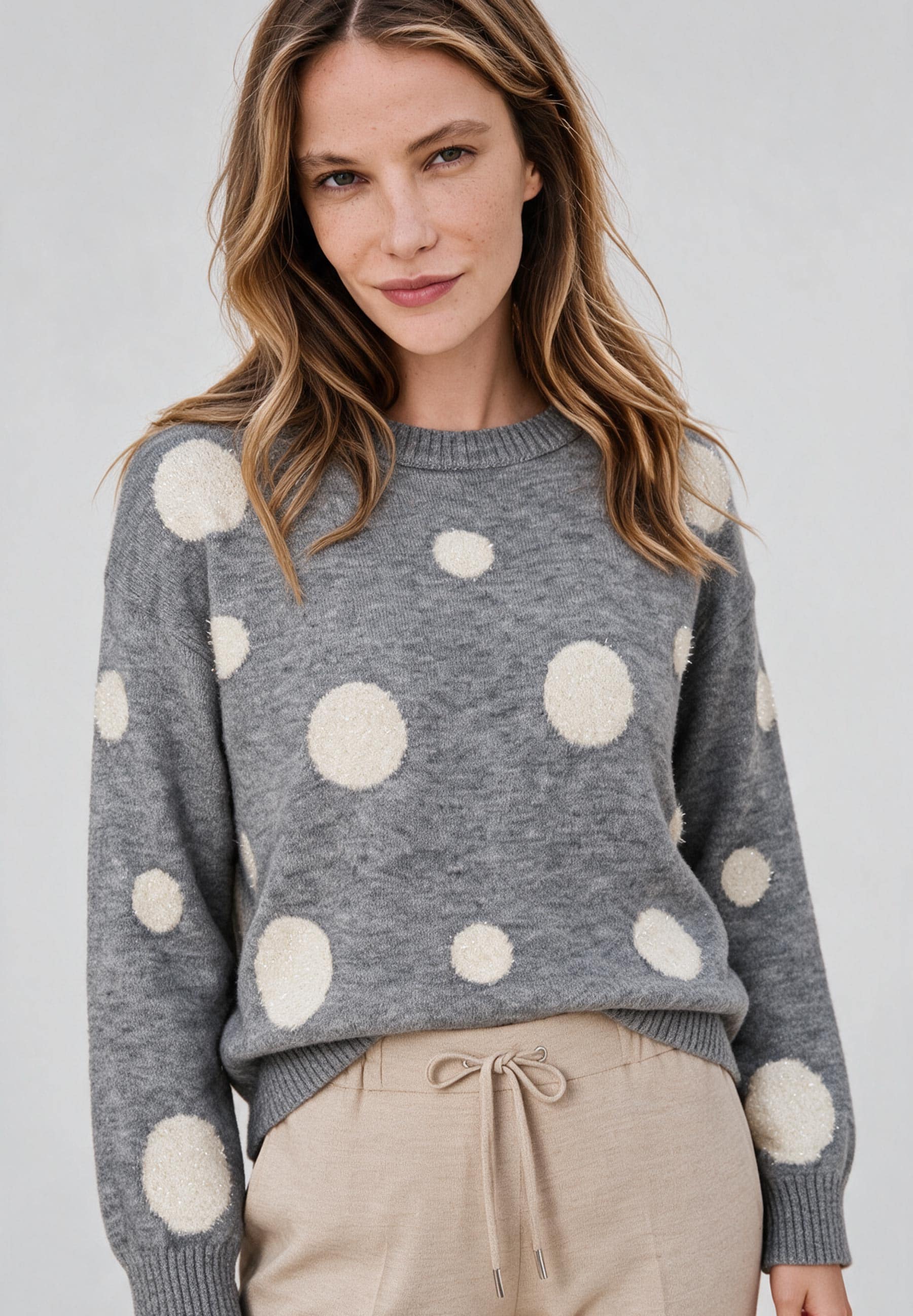 AI generated - MORE & MORE Pullover: Eine Frau trägt einen grauen Strickpullover mit beigefarbenen Punkten und eine beigefarbene Hose mit Kordelzug.