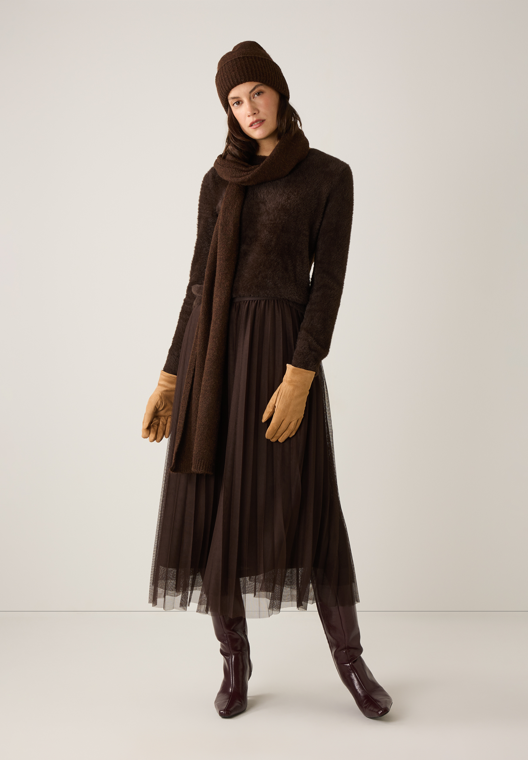 Ein Model in Strick von MORE & MORE: Mütze, Schal, Pullover, Handschuhe, Rock und Stiefel in verschiedenen Brauntönen. Ein Model in Strick von MORE & MORE: Mütze, Schal, Pullover, Handschuhe, Rock und Stiefel in verschiedenen Brauntönen.