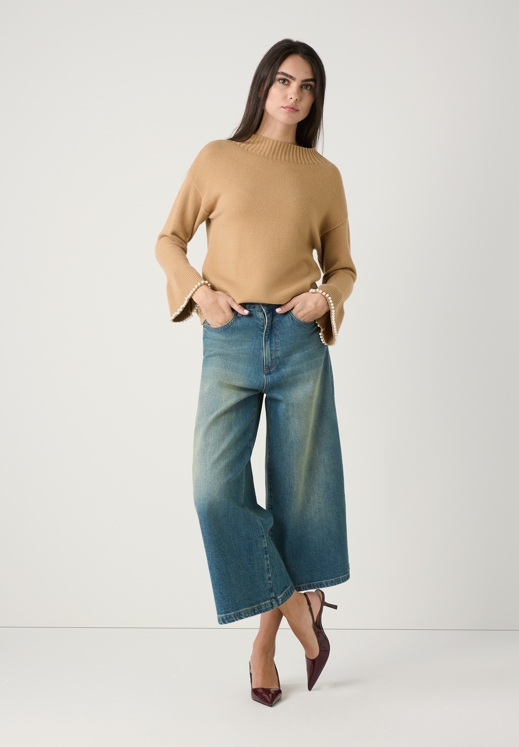 Eine Frau in MORE & MORE Oberteile und Jeans. Der Pullover ist camel-farben und hat lange Ärmel mit Perlen. Die Jeans sind weit und blau. Eine Frau in MORE & MORE Oberteile und Jeans. Der Pullover ist camel-farben und hat lange Ärmel mit Perlen. Die Jeans sind weit und blau.