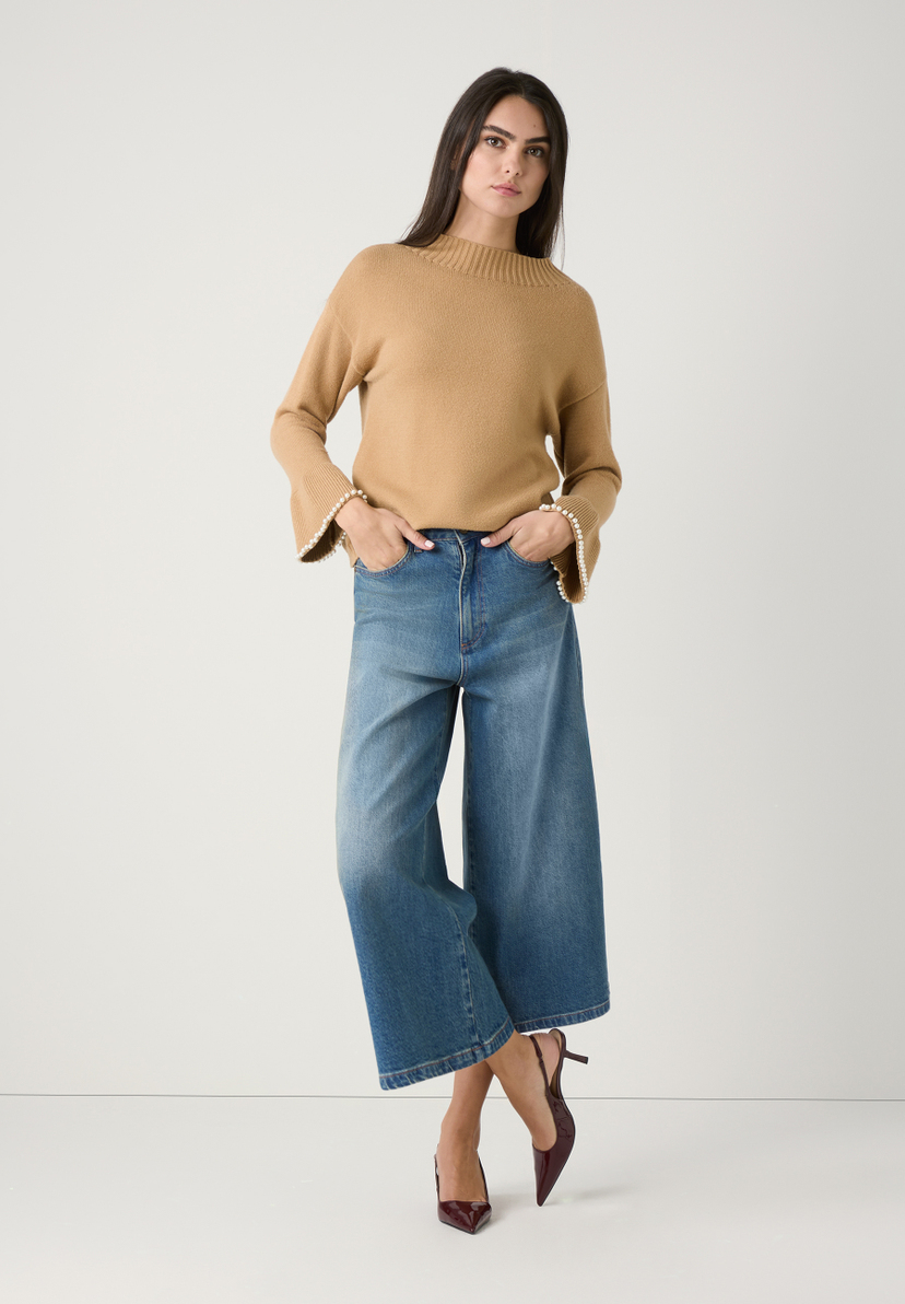 Eine Frau in MORE & MORE Strickpullover und Jeans vor einem weißen Hintergrund. Eine Frau in MORE & MORE Strickpullover und Jeans vor einem weißen Hintergrund.