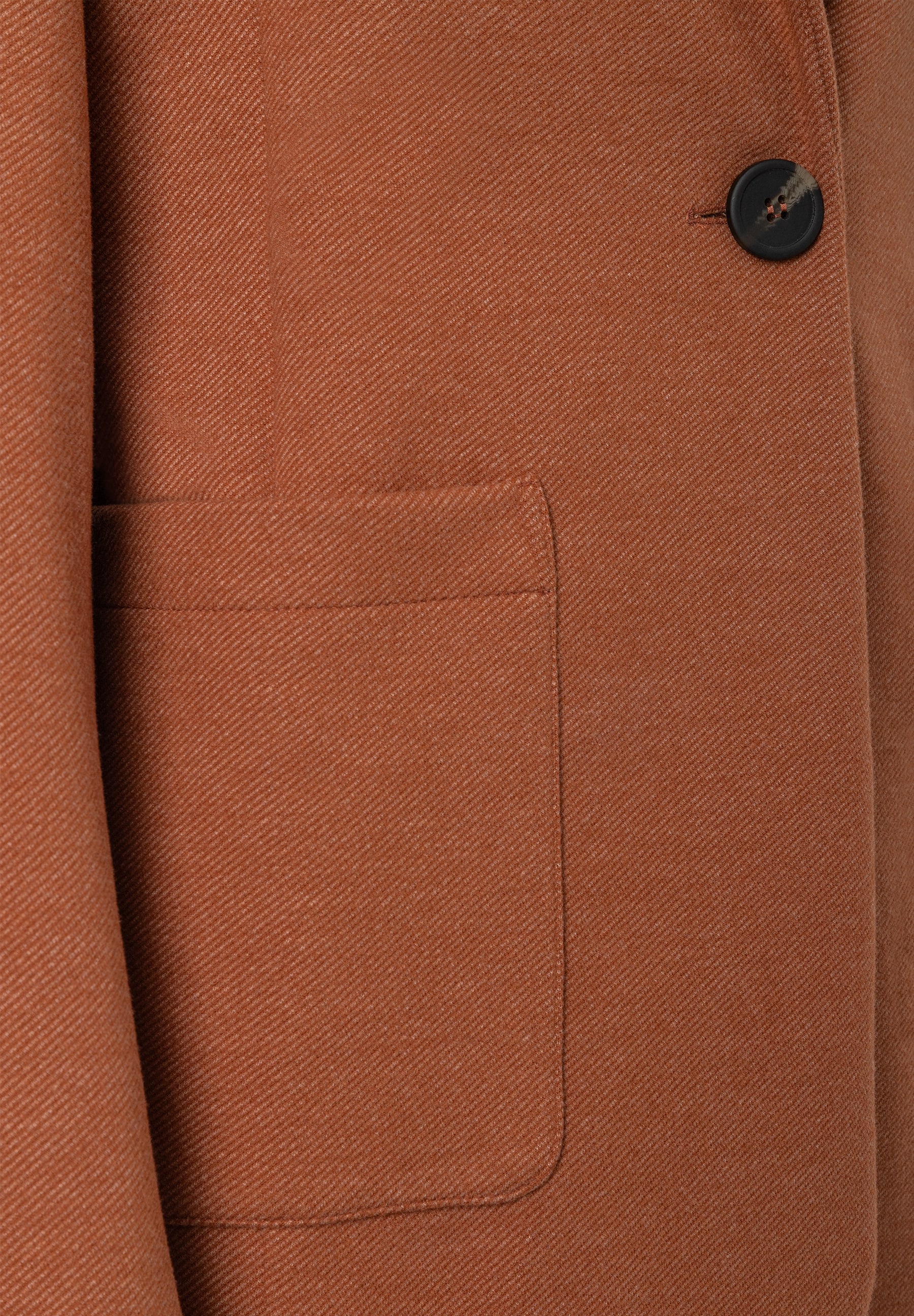 MORE & MORE Blazer in Rostbraun, Detailansicht: Stoff mit diagonalem Muster, eine Tasche und ein dunkler Knopf. MORE & MORE Blazer in Rostbraun, Detailansicht: Stoff mit diagonalem Muster, eine Tasche und ein dunkler Knopf.