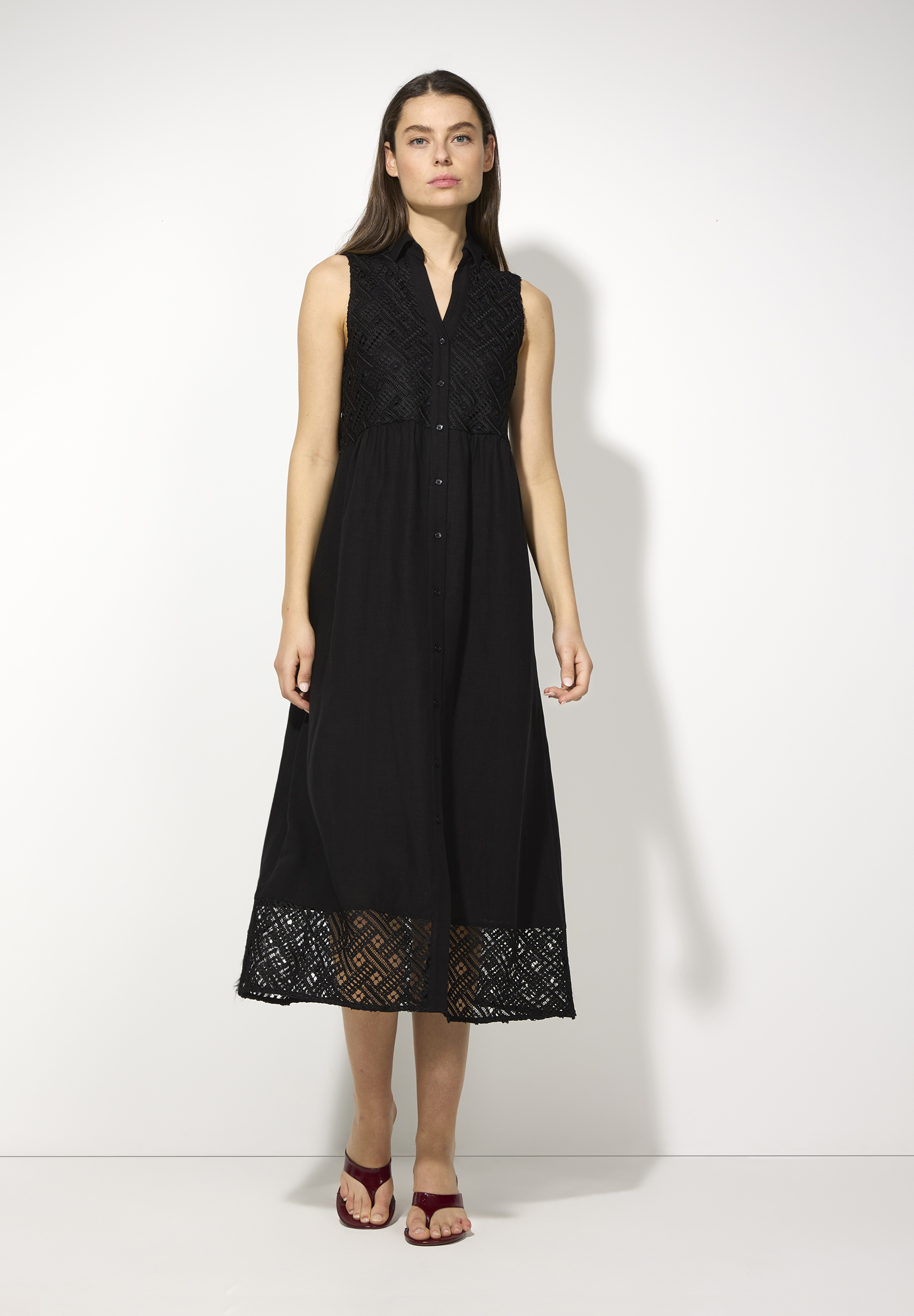 Eine Frau trägt ein ärmelloses, schwarzes MORE & MORE Kleid mit Spitze am Oberteil und Saum.
