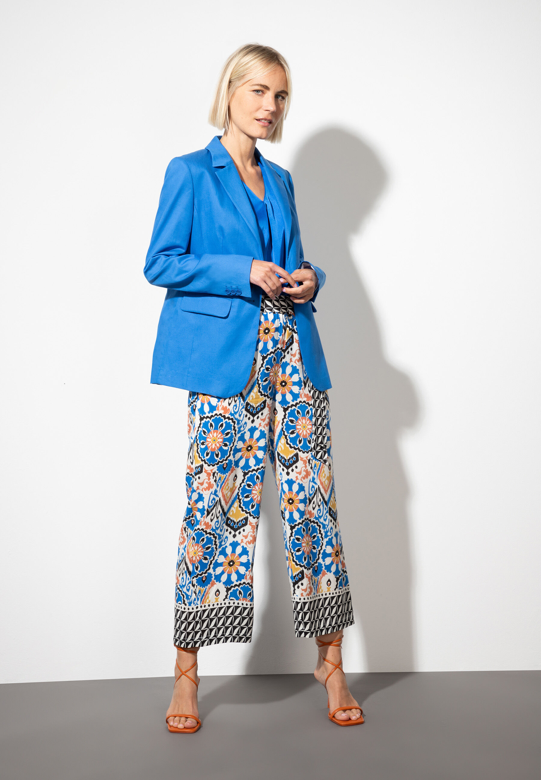 Eine Frau trägt einen blauen Blazer von MORE & MORE mit bunten Oberteilen und Absatzsandalen. Eine Frau trägt einen blauen Blazer von MORE & MORE mit bunten Oberteilen und Absatzsandalen.