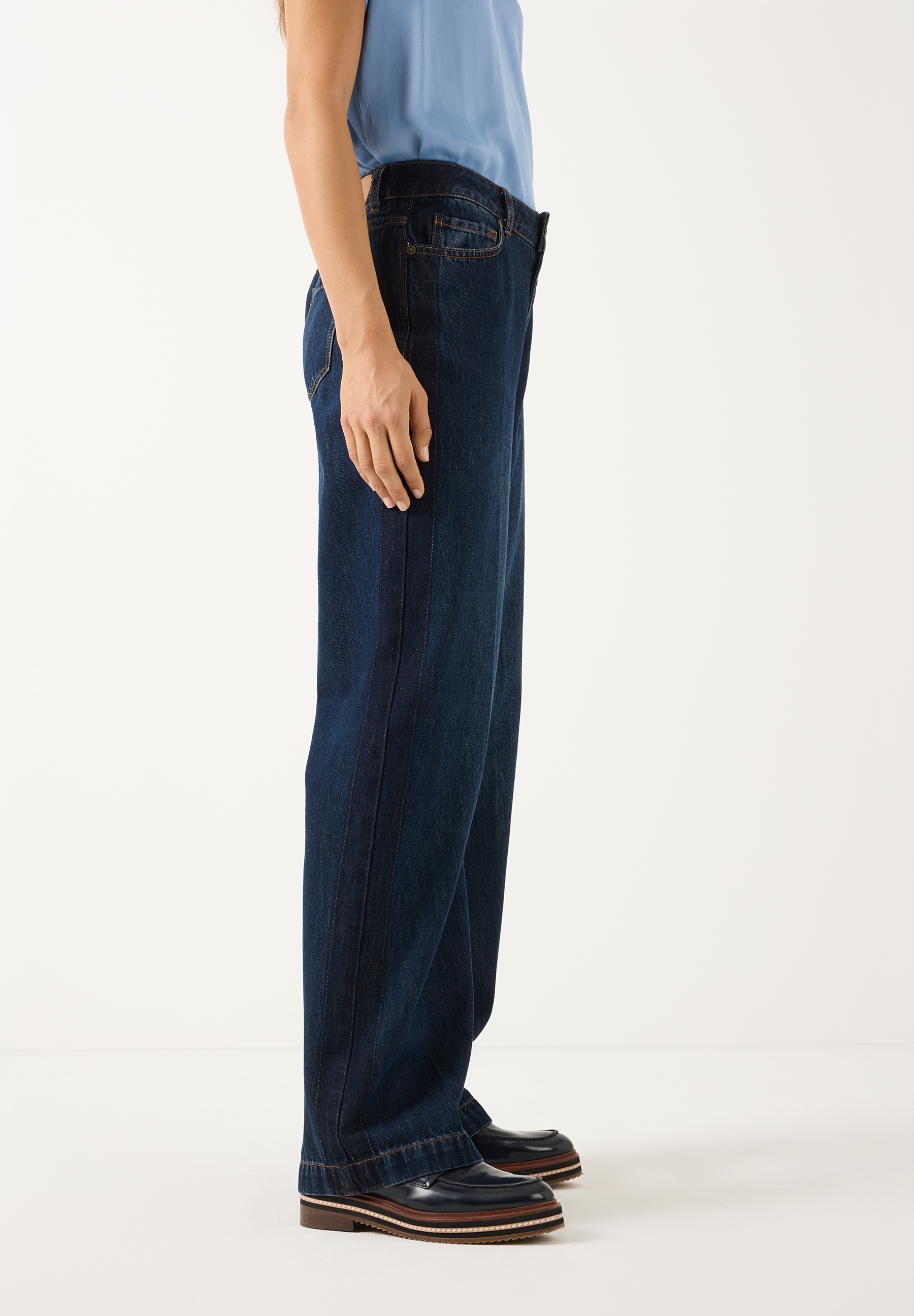 MORE & MORE Jeans: eine Person in dunkelblauen, weiten Jeans und einem hellblauen Top. Dazu trägt sie klobige, schwarze Loafer.
