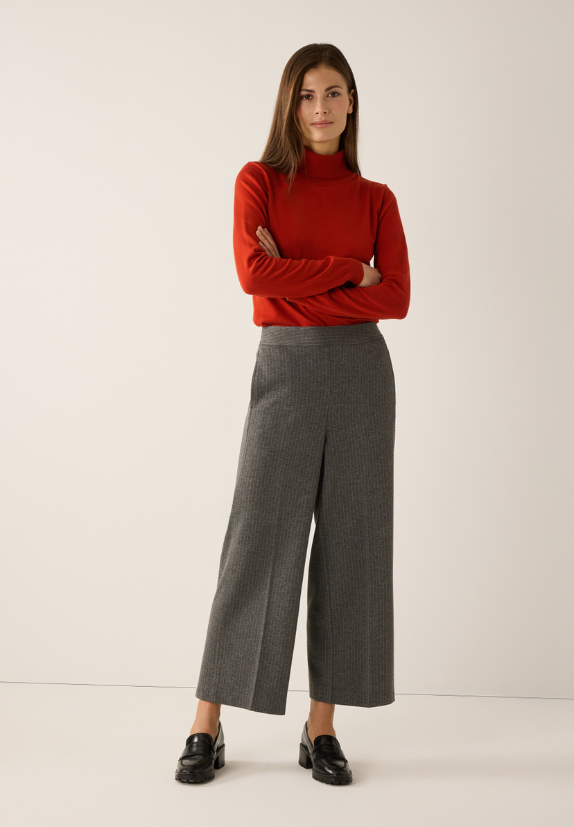 Eine Frau mit einem roten Rollkragenpullover und einer MORE & MORE Webware Hose in Grau mit Nadelstreifen. Eine Frau mit einem roten Rollkragenpullover und einer MORE & MORE Webware Hose in Grau mit Nadelstreifen.