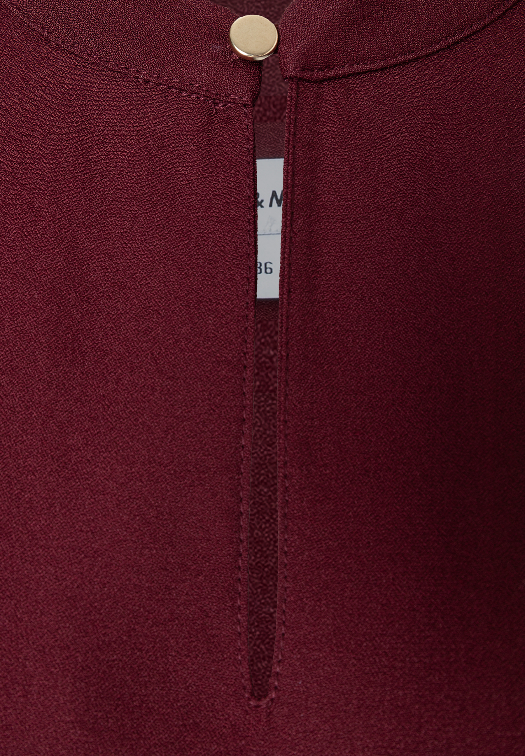 MORE & MORE Bluse: Eine Nahaufnahme der eleganten, bordeauxroten Bluse mit goldenem Knopfdetail und einem kleinen Schlitz.