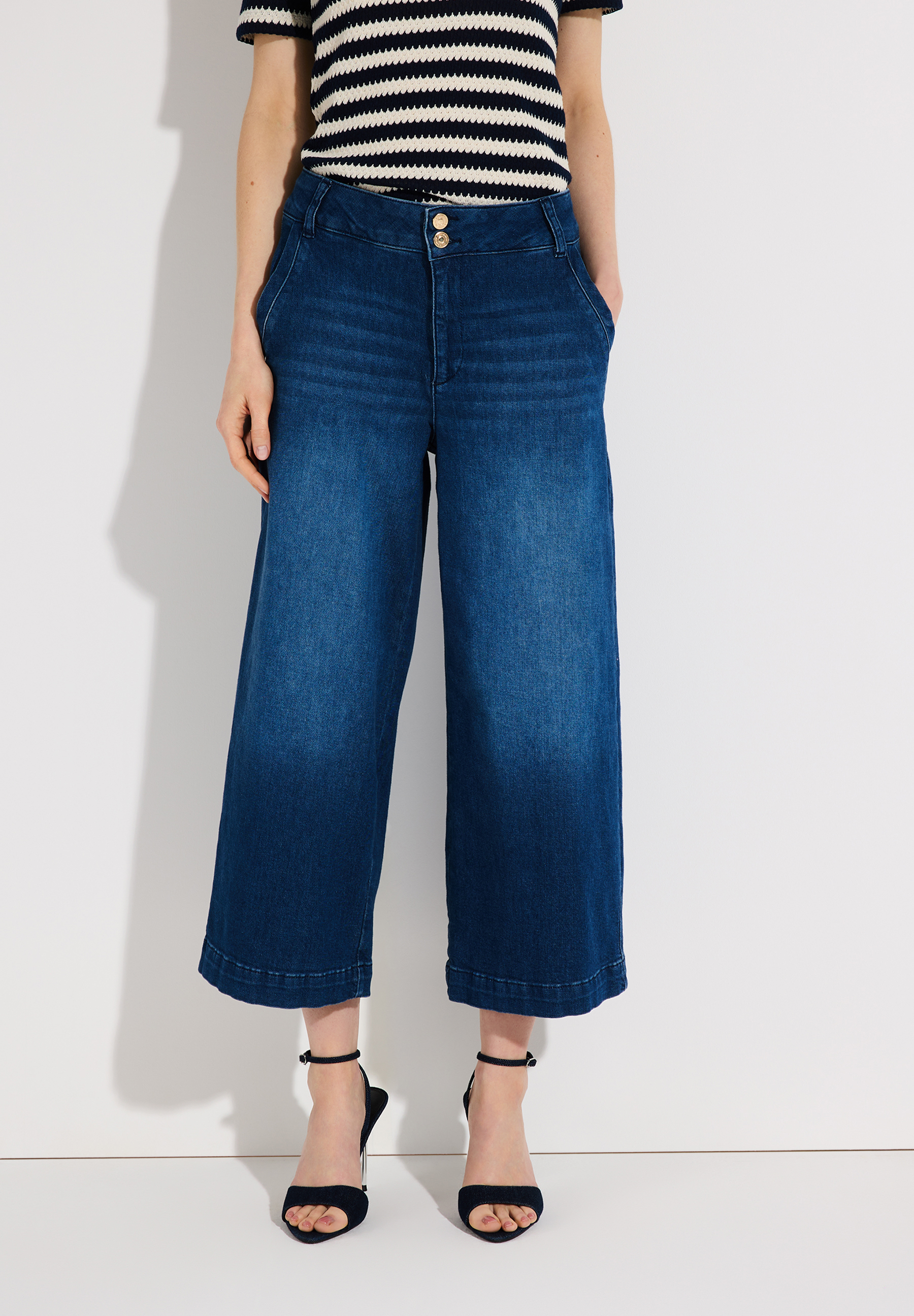 Eine Frau mit MORE & MORE Denim Jeans in Culotte-Form und silbernen Schuhen.