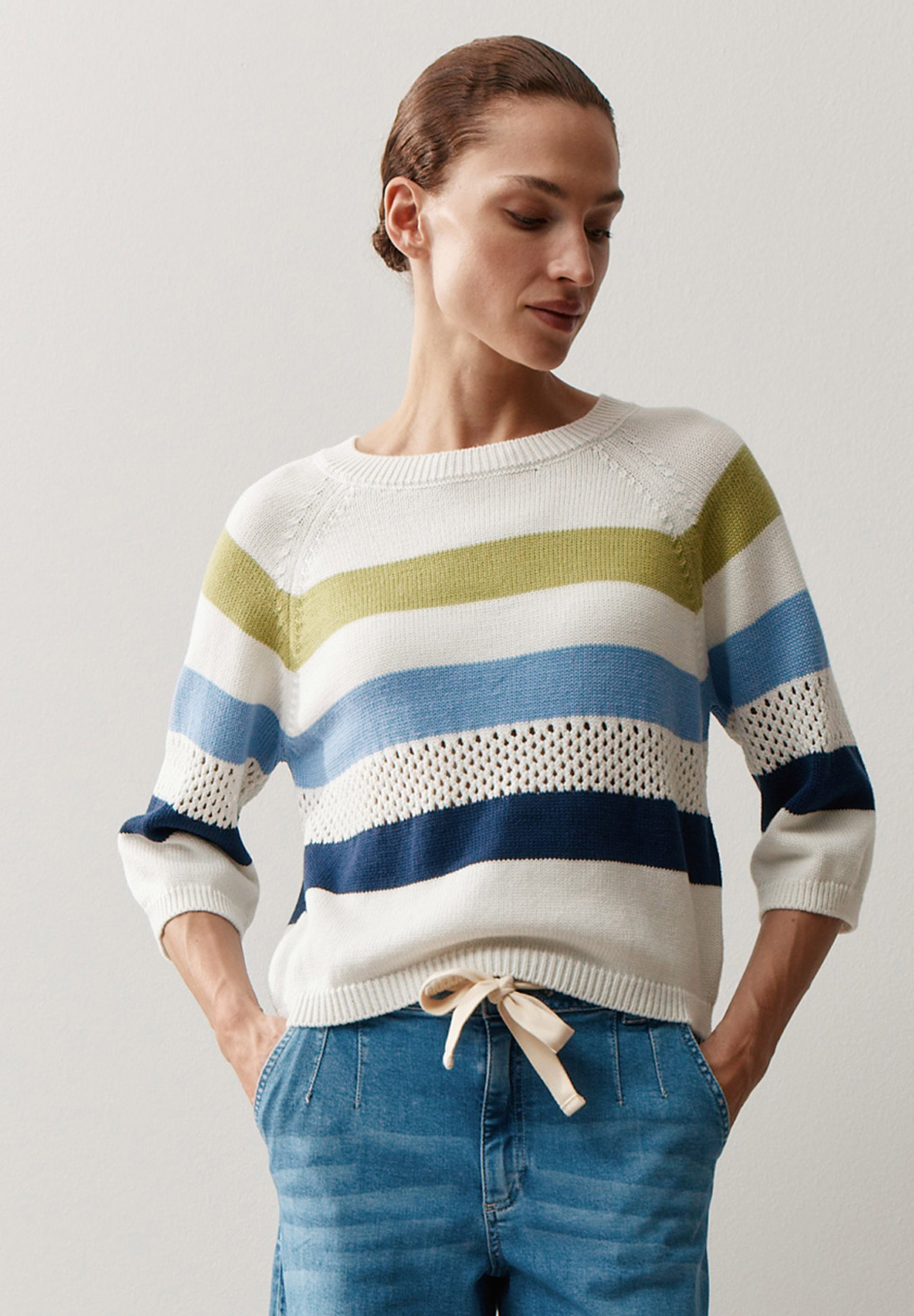 Eine Frau in einem gestreiften MORE & MORE Strickpullover mit Lochstrick und Jeans. Eine Frau in einem gestreiften MORE & MORE Strickpullover mit Lochstrick und Jeans.