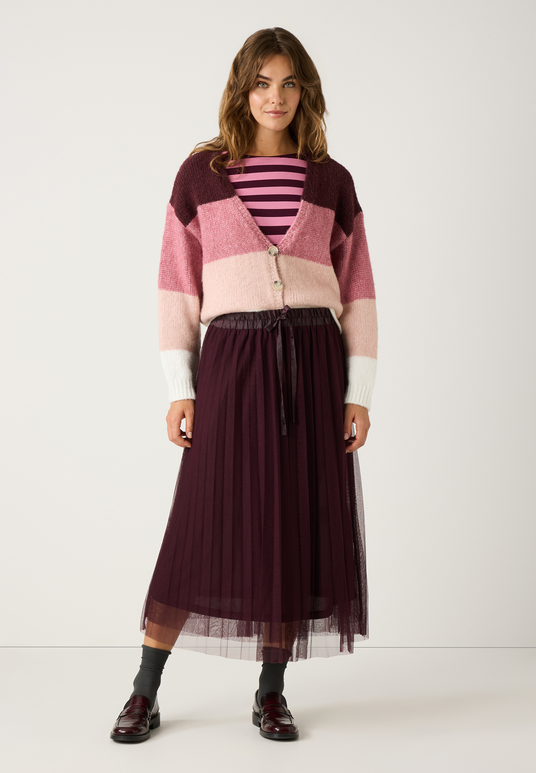 Eine Frau in einem MORE & MORE Strick-Oberteil mit rosa Streifen und passendem Rock. Eine Frau in einem MORE & MORE Strick-Oberteil mit rosa Streifen und passendem Rock.