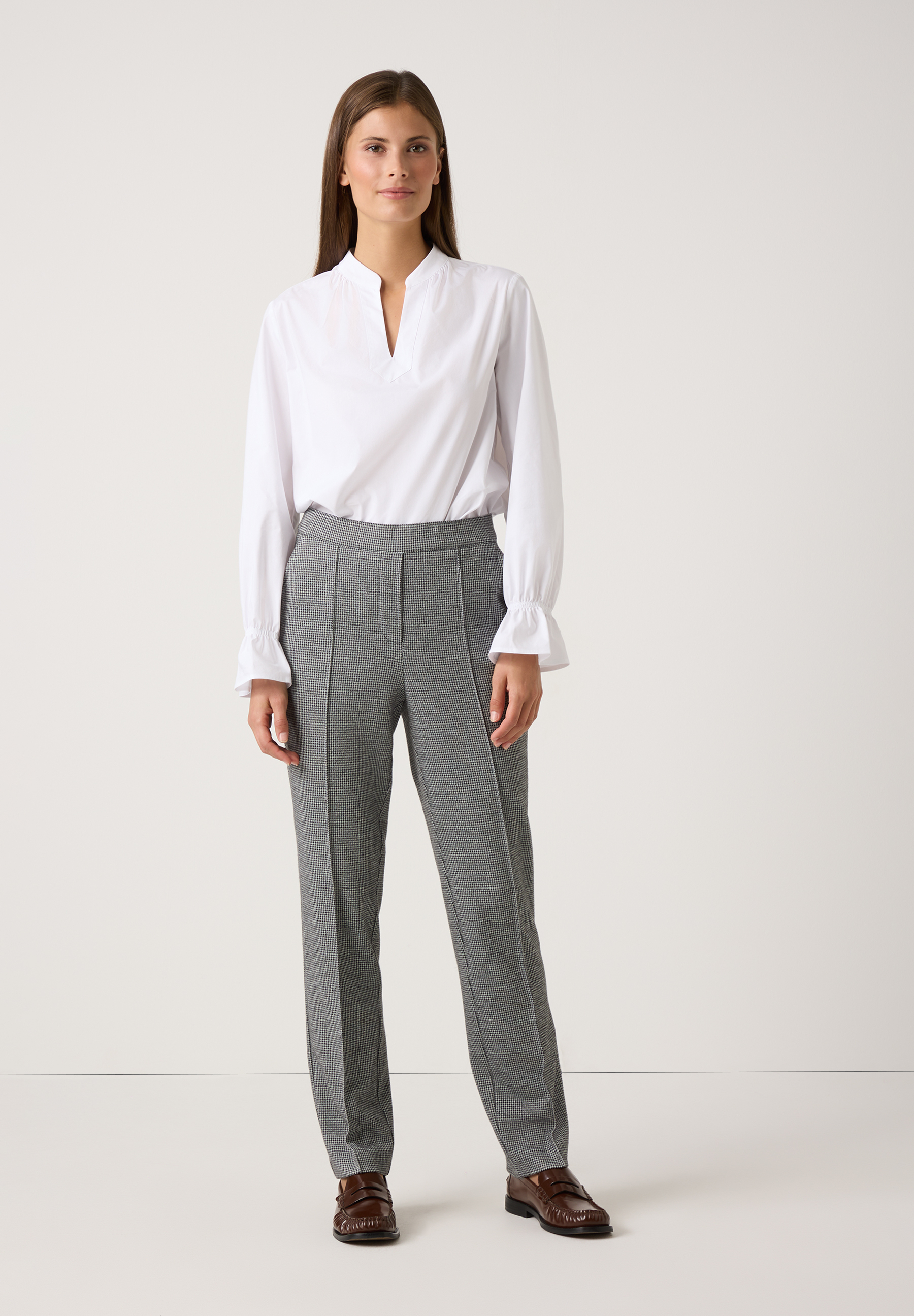 Eine Frau präsentiert MORE & MORE Jersey-Hosen mit Hahnentrittmuster zu einer weißen Bluse und braunen Schuhen. Eine Frau präsentiert MORE & MORE Jersey-Hosen mit Hahnentrittmuster zu einer weißen Bluse und braunen Schuhen.