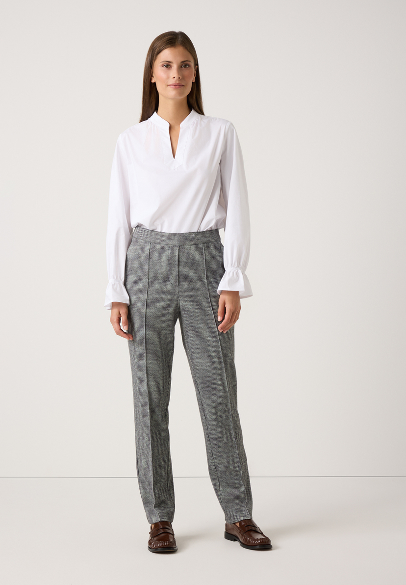 Eine Frau präsentiert MORE & MORE Jersey-Hosen mit Hahnentrittmuster zu einer weißen Bluse und braunen Schuhen. Eine Frau präsentiert MORE & MORE Jersey-Hosen mit Hahnentrittmuster zu einer weißen Bluse und braunen Schuhen.