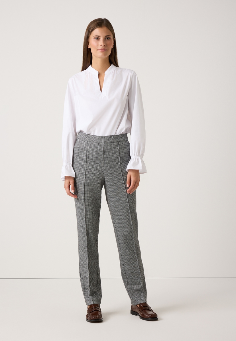Eine Frau präsentiert MORE & MORE Jersey-Hosen mit Hahnentrittmuster zu einer weißen Bluse und braunen Schuhen. Eine Frau präsentiert MORE & MORE Jersey-Hosen mit Hahnentrittmuster zu einer weißen Bluse und braunen Schuhen.