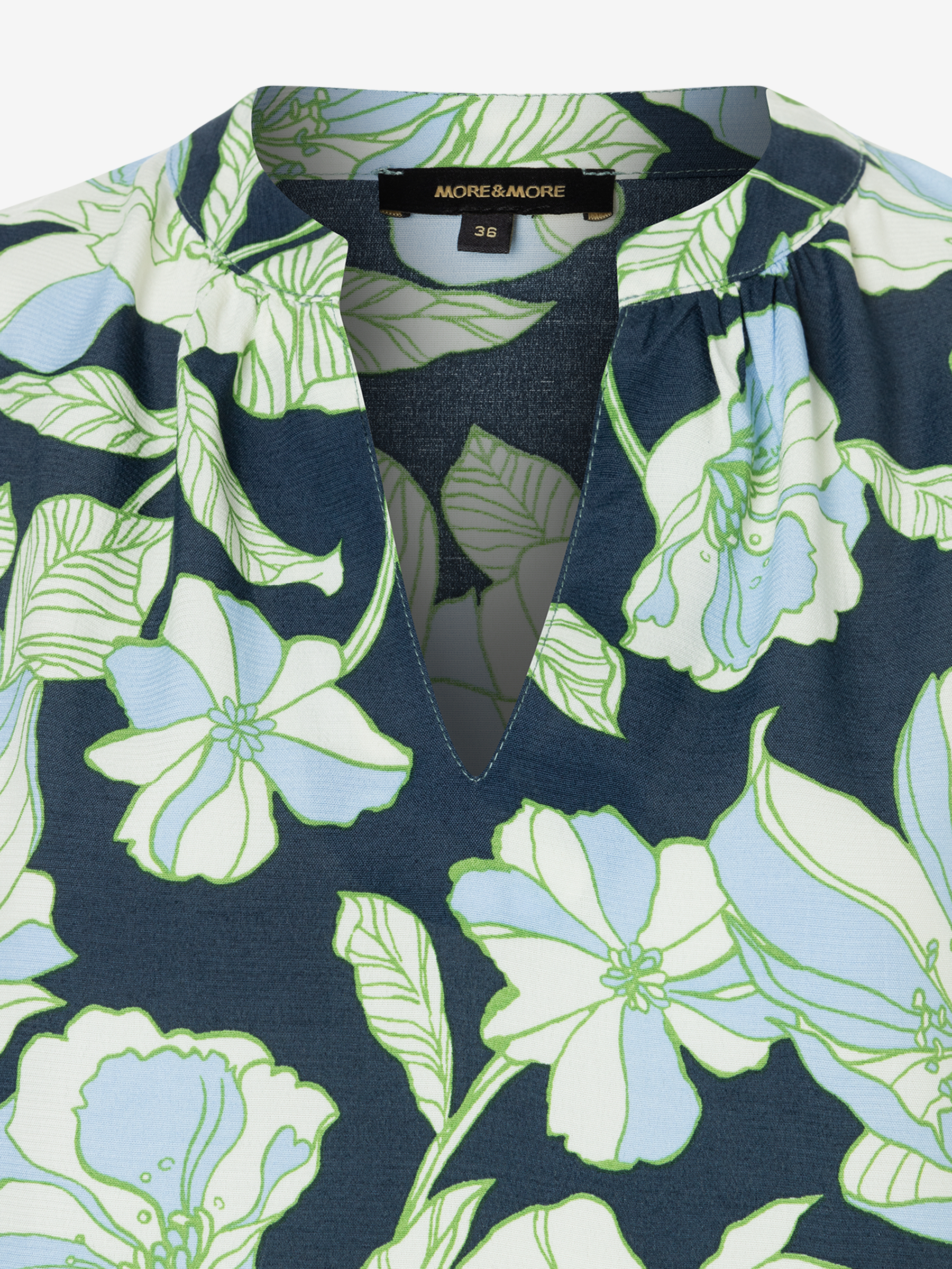 Nahaufnahme einer MORE & MORE Bluse mit blauem Blumenmuster und kleinem V-Ausschnitt. Nahaufnahme einer MORE & MORE Bluse mit blauem Blumenmuster und kleinem V-Ausschnitt.