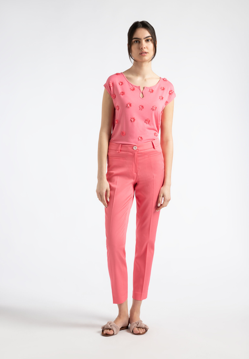 Eine Frau trägt ein korallenrotes Hosen-Outfit von MORE & MORE vor einem weißen Hintergrund. Eine Frau trägt ein korallenrotes Hosen-Outfit von MORE & MORE vor einem weißen Hintergrund.