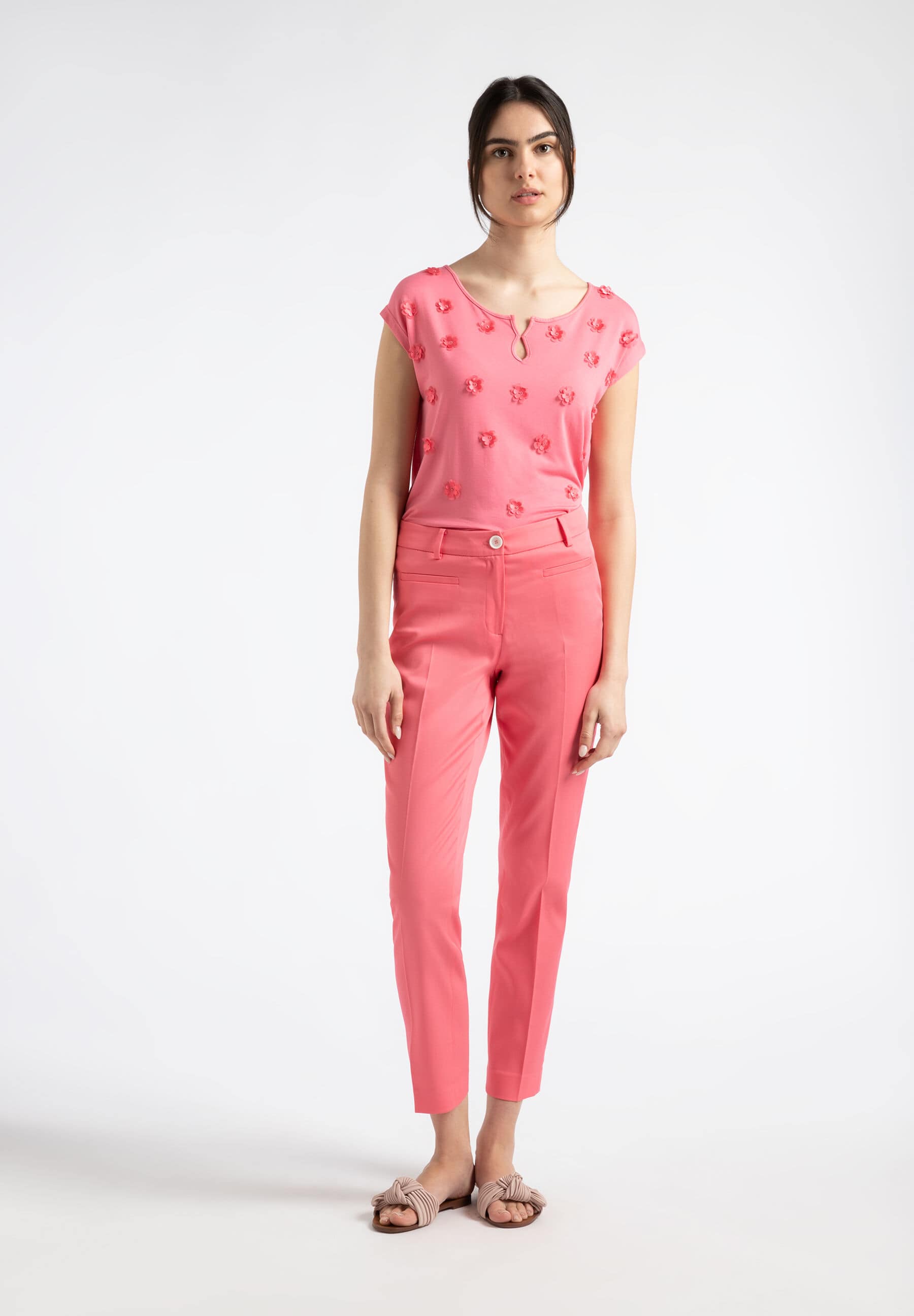 Eine Frau trägt ein korallenrotes Hosen-Outfit von MORE & MORE vor einem weißen Hintergrund. Eine Frau trägt ein korallenrotes Hosen-Outfit von MORE & MORE vor einem weißen Hintergrund.