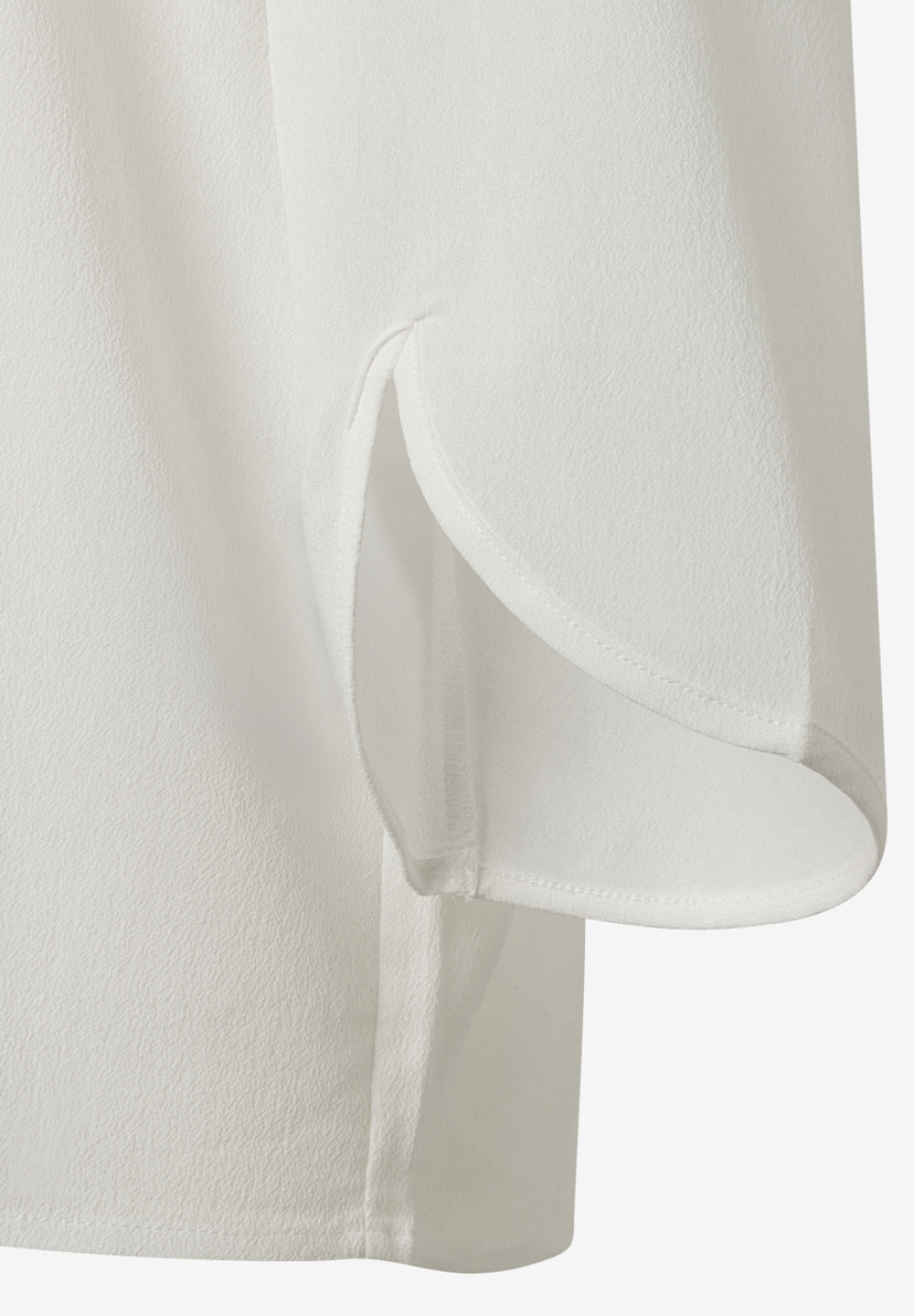 Nahaufnahme einer weißen MORE & MORE Bluse aus Viskose-Crêpe-Webware mit Seitenschlitz. Nahaufnahme einer weißen MORE & MORE Bluse aus Viskose-Crêpe-Webware mit Seitenschlitz.