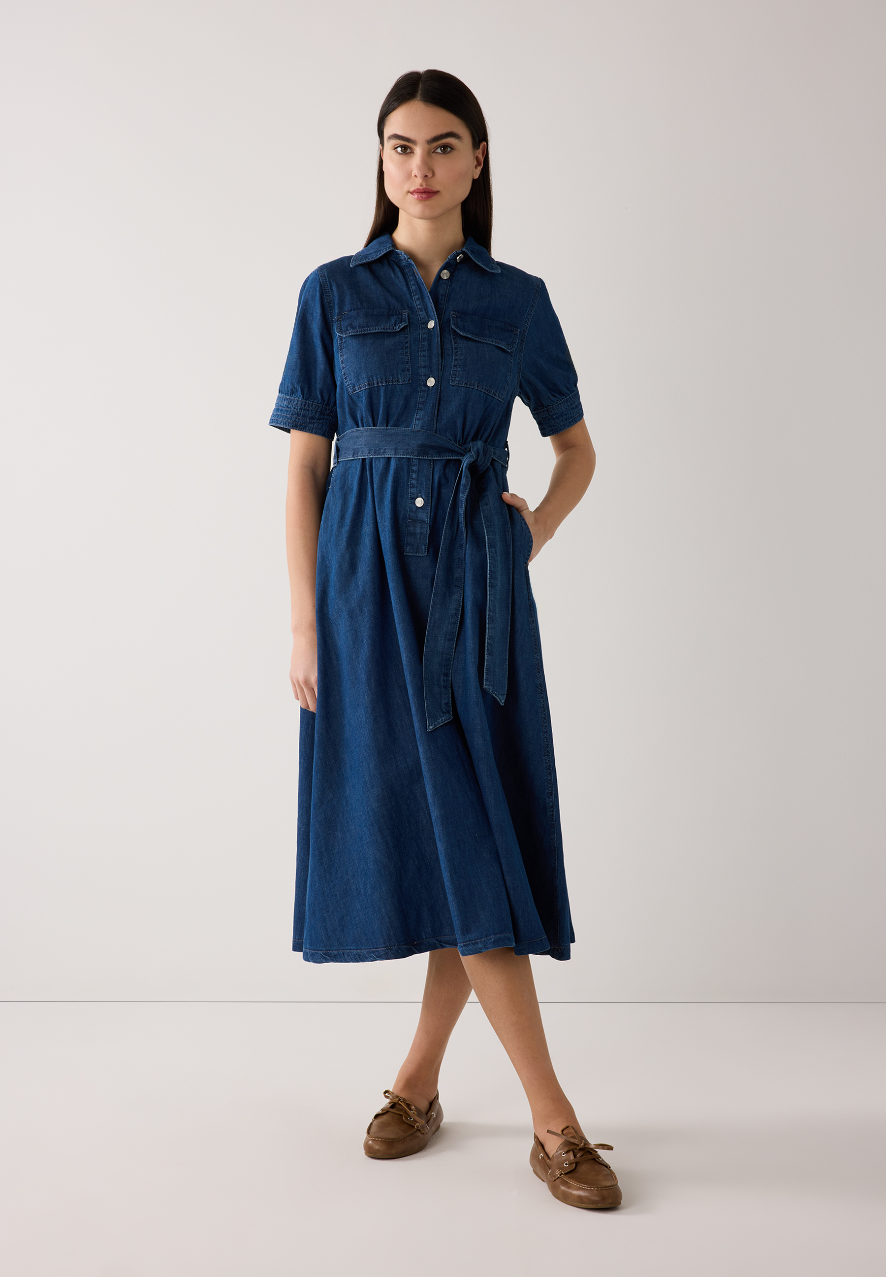 Eine Frau im MORE & MORE Jeans-Hemdkleid mit Gürtel und bequemer Denim-Konstruktion. Eine Frau im MORE & MORE Jeans-Hemdkleid mit Gürtel und bequemer Denim-Konstruktion.
