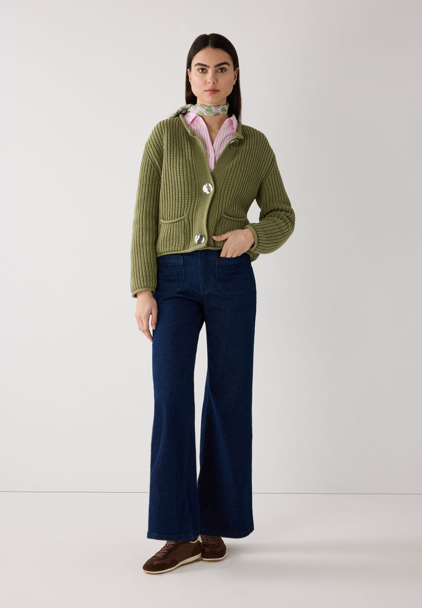 Eine Frau in MORE & MORE Strickware trägt ein grünes Rippstrick-Oberteil, eine gestreifte Bluse, weite Jeans und braune Schuhe. Eine Frau in MORE & MORE Strickware trägt ein grünes Rippstrick-Oberteil, eine gestreifte Bluse, weite Jeans und braune Schuhe.