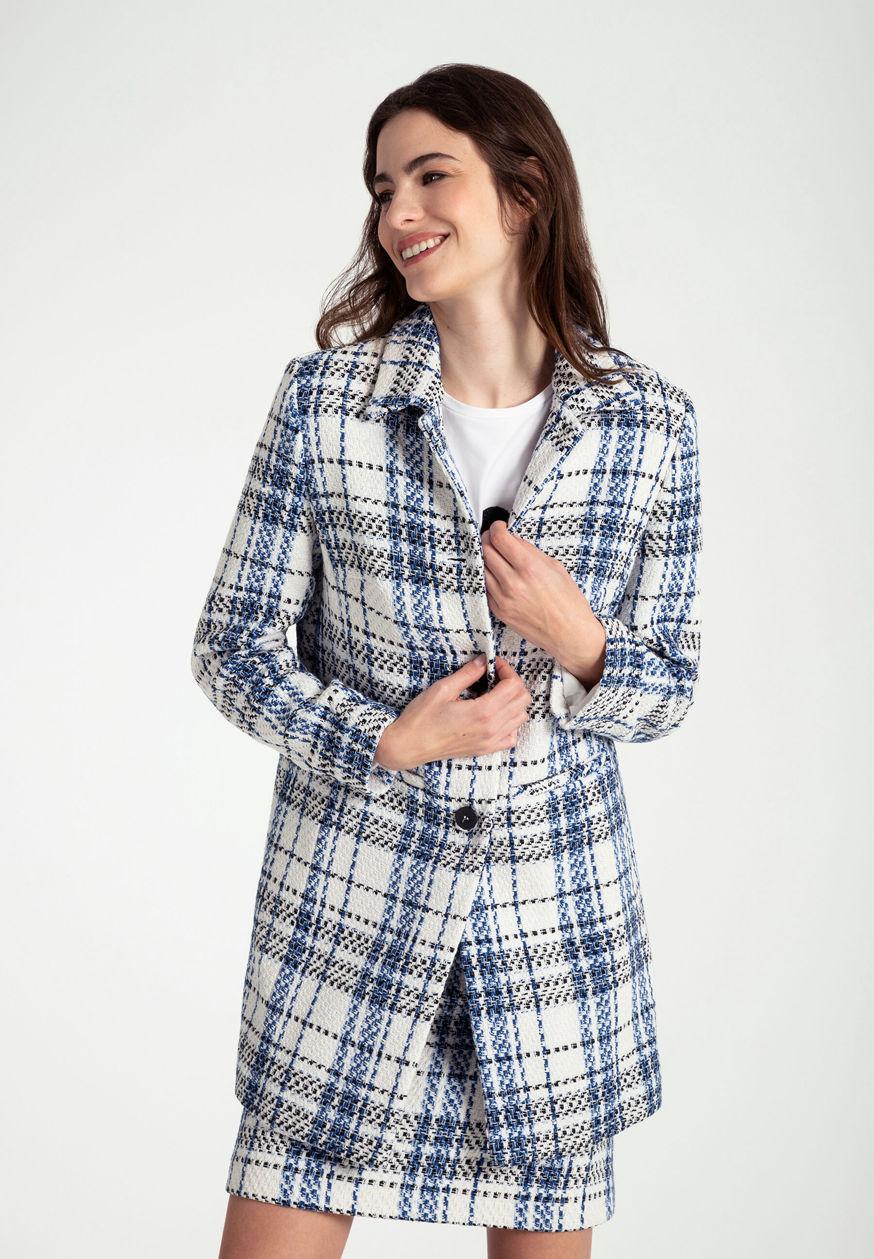 Eine lächelnde Frau mit einem karierten MORE & MORE Bouclé-Blazer. Sie ist vor einem weißen Hintergrund zu sehen.