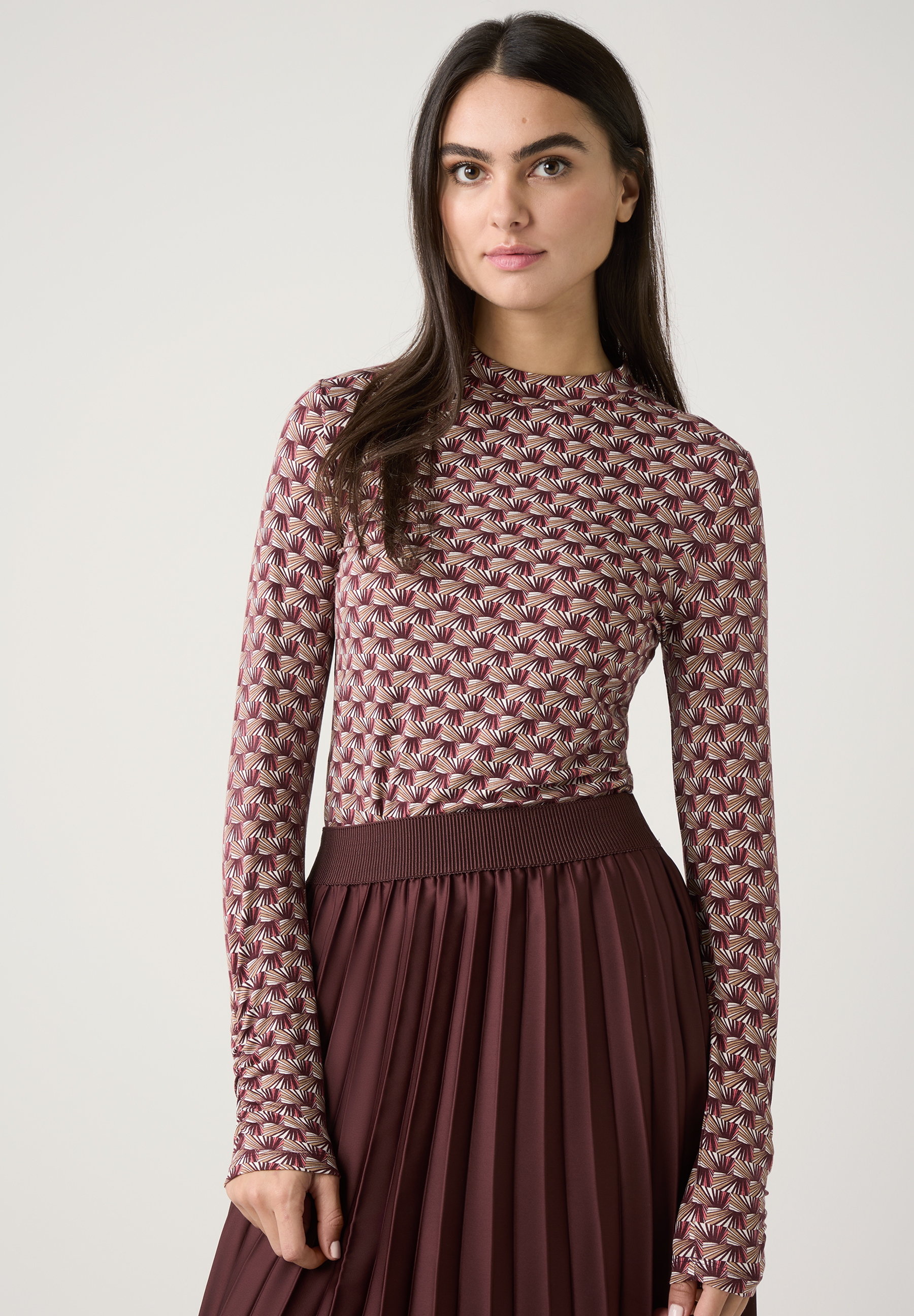 Eine Frau trägt ein gemustertes Oberteil von MORE & MORE und einen braunen Faltenrock. Eine Frau trägt ein gemustertes Oberteil von MORE & MORE und einen braunen Faltenrock.