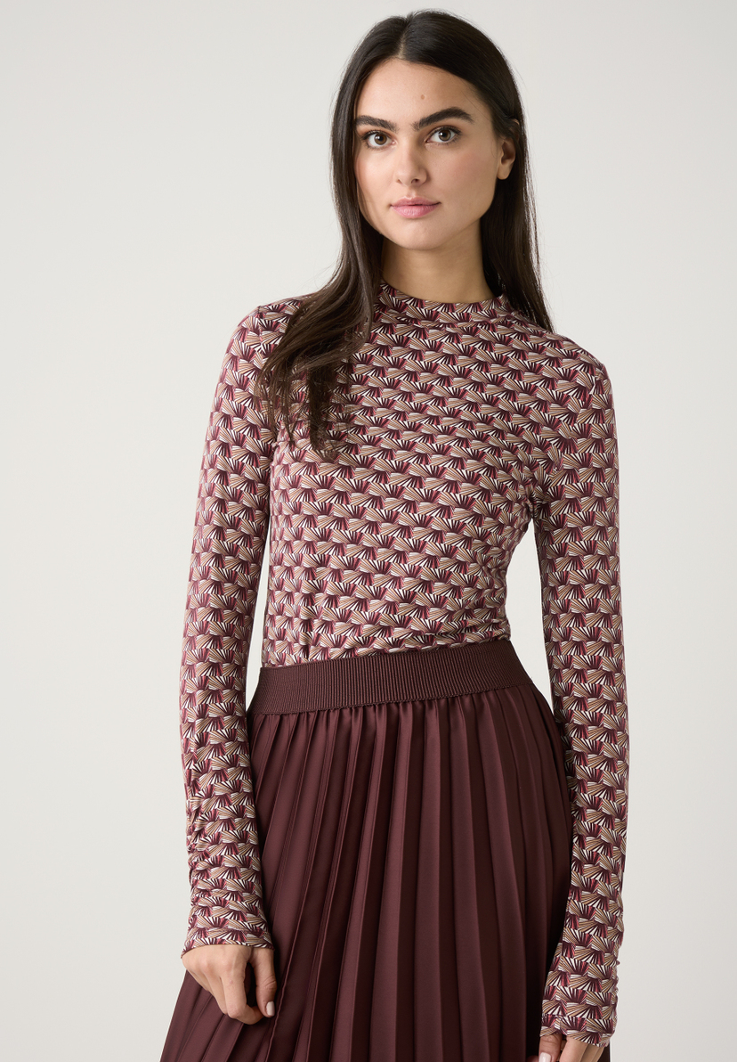 Eine Frau trägt ein gemustertes Oberteil von MORE & MORE und einen braunen Faltenrock. Eine Frau trägt ein gemustertes Oberteil von MORE & MORE und einen braunen Faltenrock.